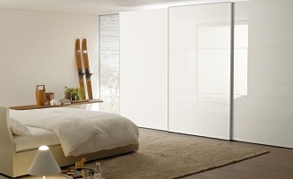 Bílá skleněná šatní skřín s posuvnými dveřmi v ložnici